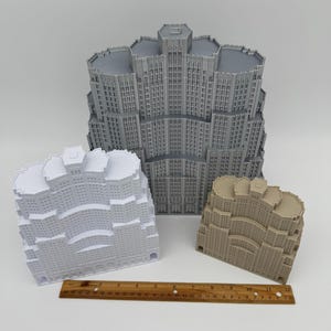 May include: Three miniature building models in grey, white, and tan, with a wooden ruler. The buildings have detailed facades with windows and architectural features. The ruler is approximately 30 cm long.