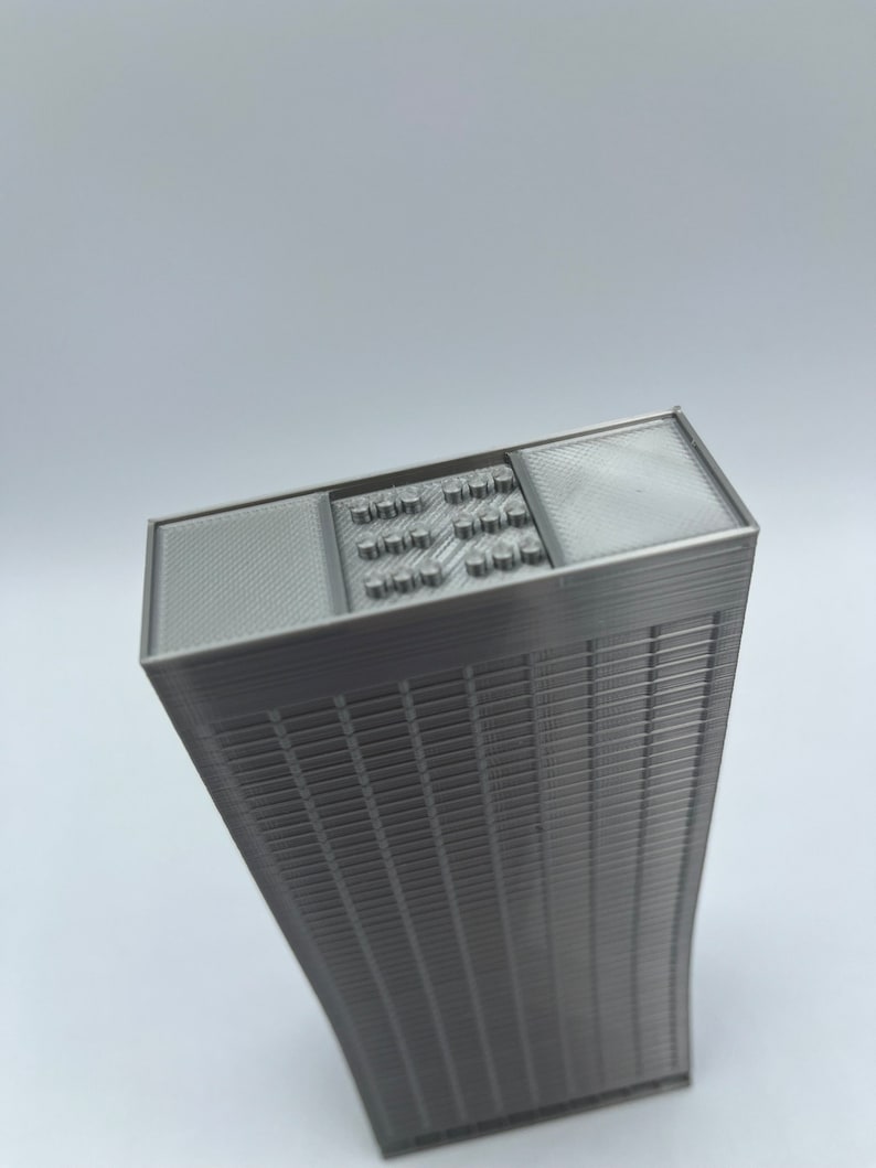 May include: A 3D printed model of a skyscraper with a detailed facade and a flat roof with a grid pattern.
