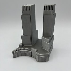 Op de afbeelding: Een 3D-geprint model van een moderne wolkenkrabber met twee torens en een basis. Het model is gemaakt van grijs plastic en heeft een gedetailleerd ontwerp.
