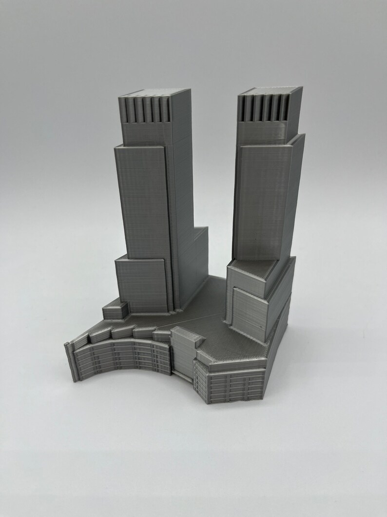 Op de afbeelding: Een 3D-geprint model van een moderne wolkenkrabber met twee torens en een basis. Het model is gemaakt van grijs plastic en heeft een gedetailleerd ontwerp.