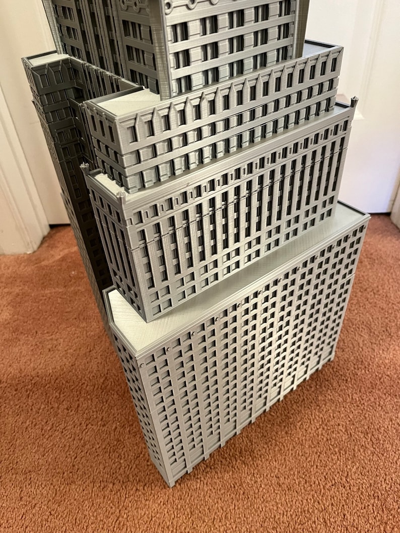 May include: A detailed model of a skyscraper, made of gray plastic, with multiple levels and windows. The model is angled to show the side of the building.