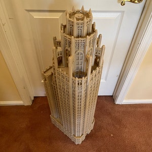 May include: A detailed model of a tall, beige building with a pointed roof and intricate architectural details. The model is made of plastic and appears to be a replica of a famous skyscraper.