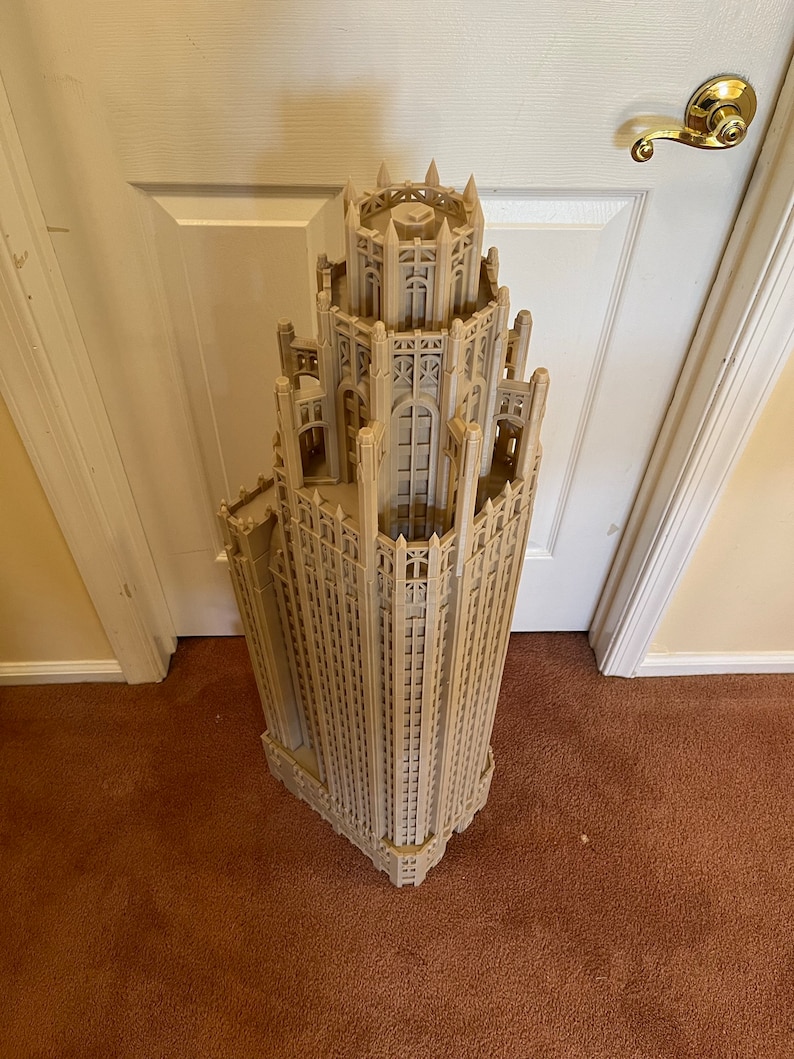 May include: A detailed model of a tall, beige building with a pointed roof and intricate architectural details. The model is made of plastic and appears to be a replica of a famous skyscraper.