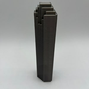 May include: A dark gray 3D printed model of a skyscraper with a stepped design.