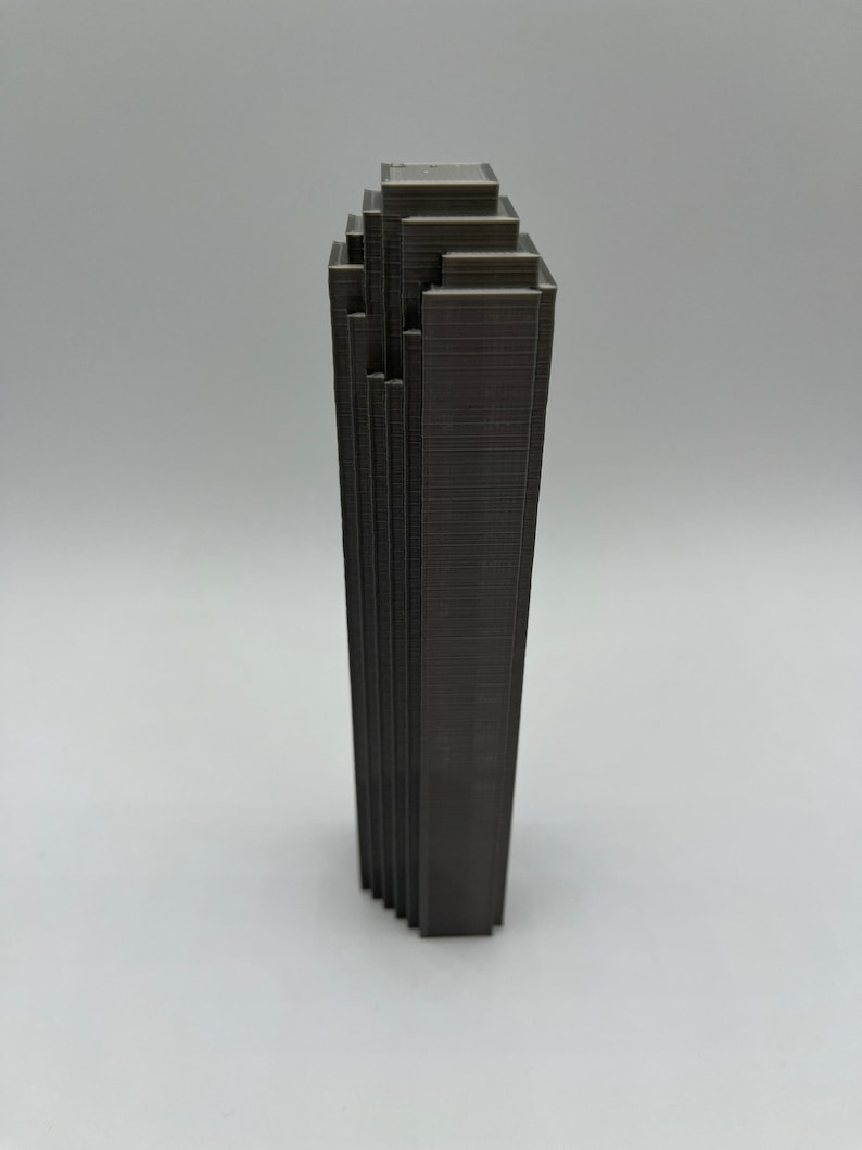 May include: A dark gray 3D printed model of a skyscraper with a stepped design.