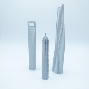 May include: Three silver 3D printed models of skyscrapers. The models are of different shapes and sizes. The tallest model is a curved skyscraper, the middle model is a tall, thin skyscraper, and the shortest model is a square skyscraper.
