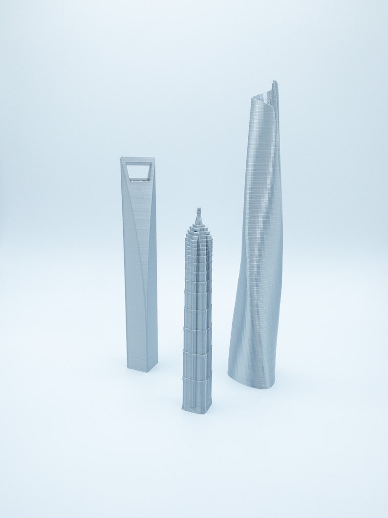 May include: Three silver 3D printed models of skyscrapers. The models are of different shapes and sizes. The tallest model is a curved skyscraper, the middle model is a tall, thin skyscraper, and the shortest model is a square skyscraper.
