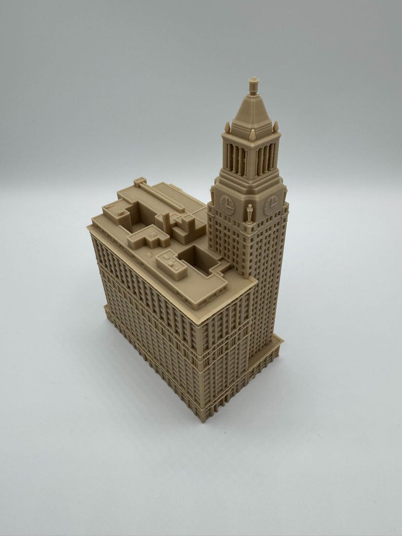 May include: A tan-colored architectural model of a tall building with a tower. The model has detailed windows and architectural features. The building's design includes a tower with a spire, and a rectangular base.