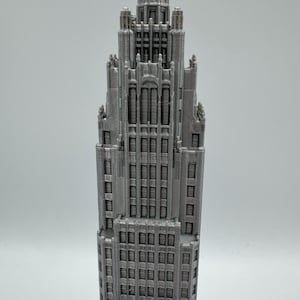 May include: A detailed, gray model of a skyscraper with a tiered design. The building features numerous windows and architectural details, showcasing a classic, ornate style. The model is a miniature representation of a famous building.