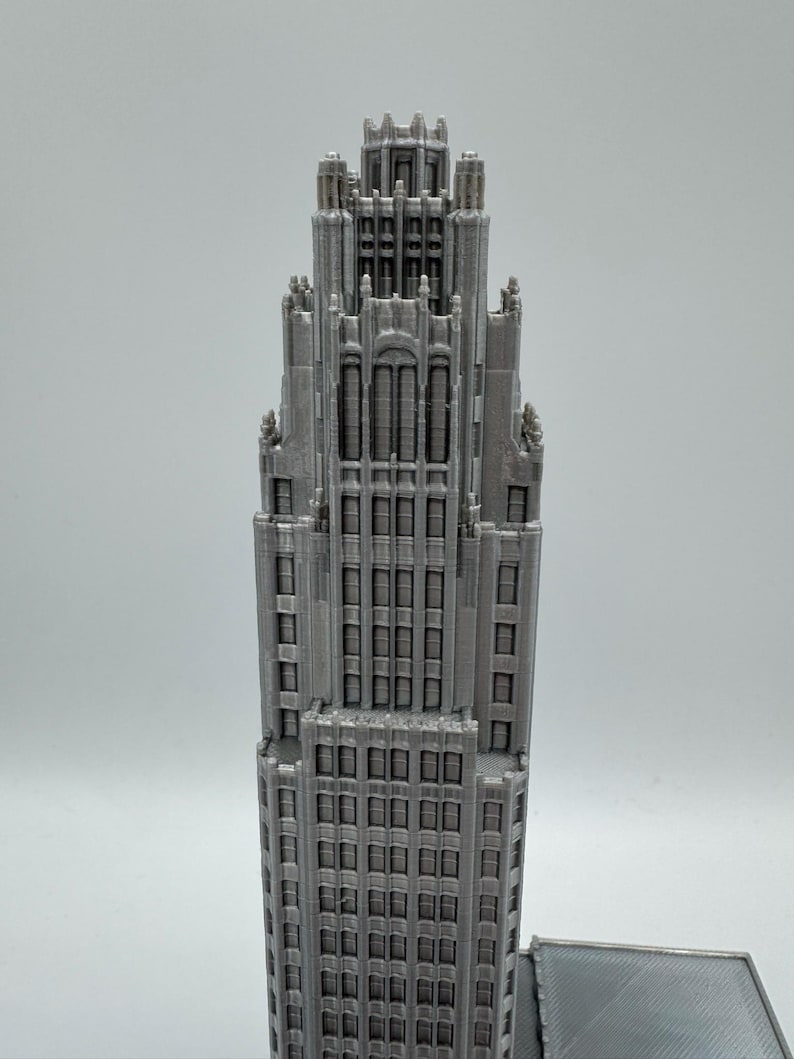 May include: A detailed, gray model of a skyscraper with a tiered design. The building features numerous windows and architectural details, showcasing a classic, ornate style. The model is a miniature representation of a famous building.
