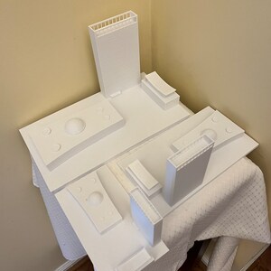 K&ouml;nnte beinhalten: Ein wei&szlig;es 3D-gedrucktes Modell einer Skyline mit mehreren Geb&auml;uden und einer Kuppelstruktur. Das Modell steht auf einer wei&szlig;en Oberfl&auml;che.