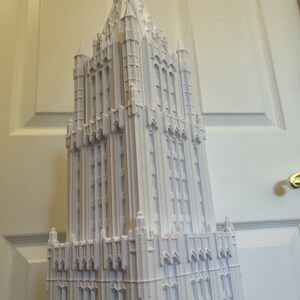 May include: A white 3D printed model of a tall, ornate building with a pointed roof and many windows.