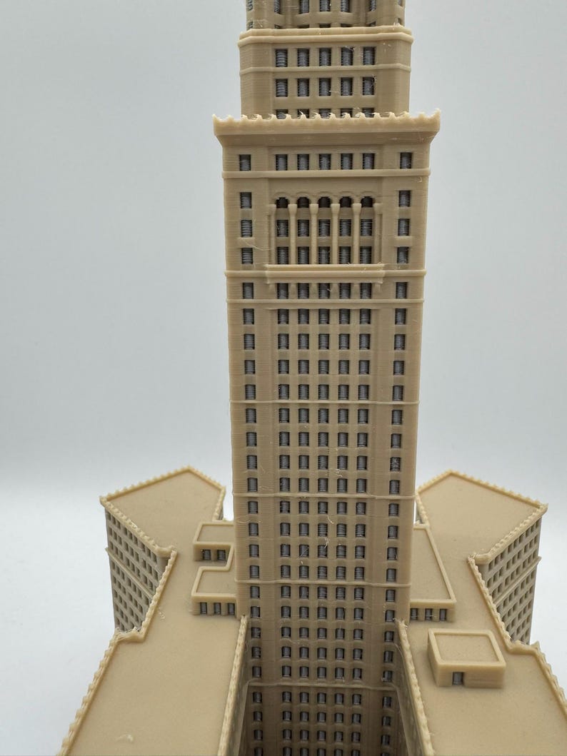 May include: A beige architectural model of a tall building with multiple stories and rectangular windows. The building has a central tower and several lower wings, all in a similar color and style. The model is likely a replica of a famous landmark.