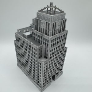 May include: A gray, 3D-printed model of a skyscraper. The building features a detailed facade with numerous windows and architectural details. The top of the building has the text "EASTERN" printed on it.