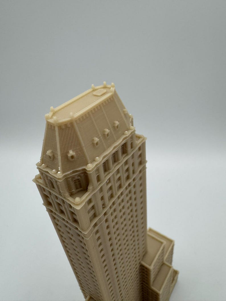 Może przedstawiać: Beżowy, drukowany w 3D model wysokiego budynku ze szczeg&oacute;łową fasadą i charakterystycznym dachem. Budynek posiada wiele okien i detali architektonicznych, prezentujących klasyczny projekt wieżowca.