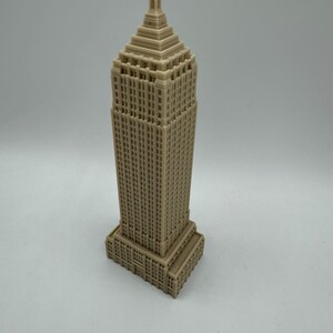 Puede incluir: Un modelo de rascacielos impreso en 3D de color beige con un techo puntiagudo y muchas ventanas.