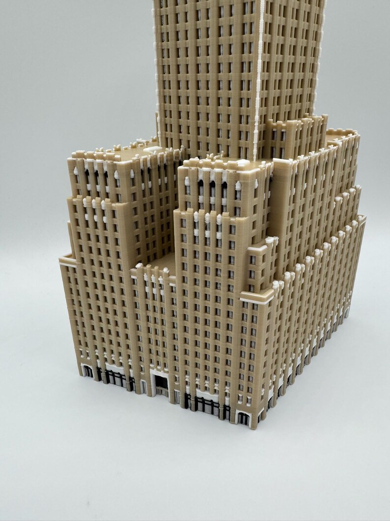 May include: A tan-coloured, multi-storey building model with a detailed facade. The model features numerous windows and architectural details, with a tiered design. The building has a light brown colour with white accents.