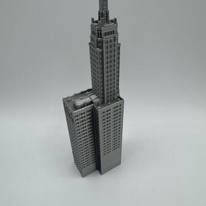May include: A grey 3D printed model of a tall skyscraper building with a pointed roof.