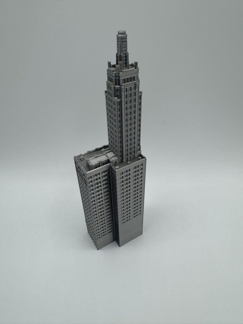 May include: A grey 3D printed model of a tall skyscraper building with a pointed roof.