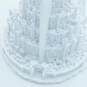 May include: White 3D printed model of a tall, multi-level structure with intricate details. The model is made of a smooth, white plastic and has a circular base.