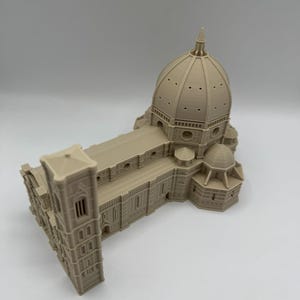 May include: A beige architectural model of a cathedral, featuring a large dome, rectangular structure, and a bell tower. The model is detailed with windows, arches, and other architectural elements. The model is a miniature replica of a famous building.