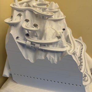 May include: A white 3D printed model of a mountain with a winding track that goes up and down the mountain.