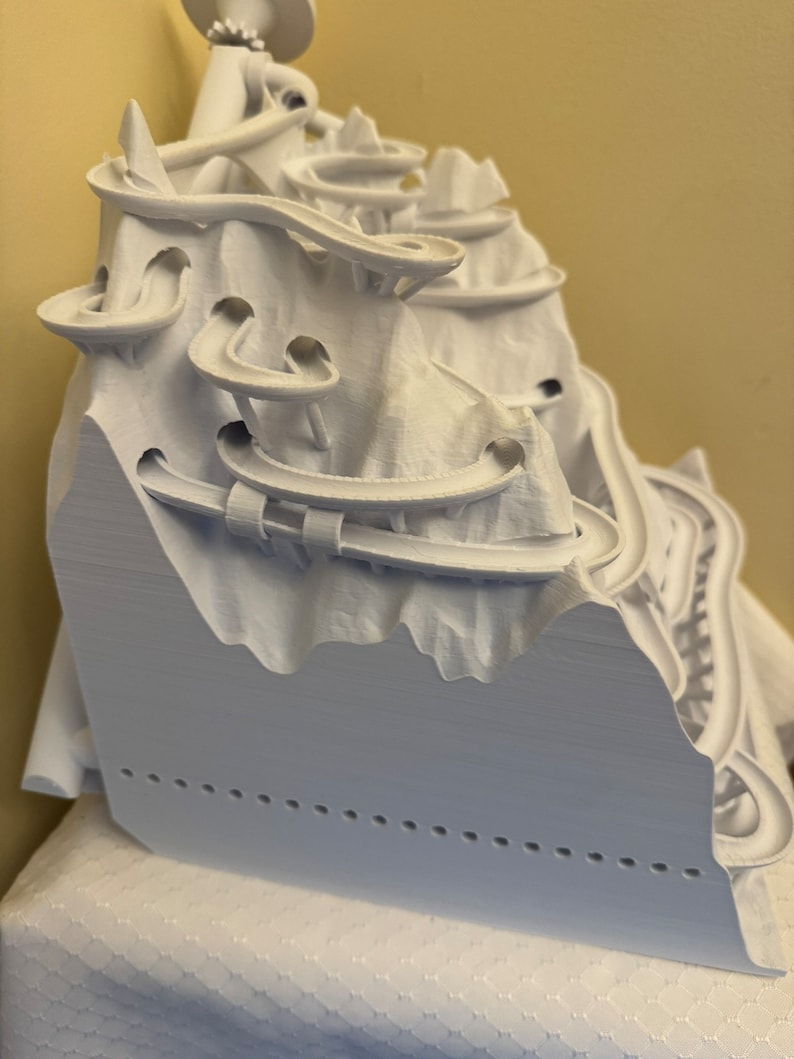 May include: A white 3D printed model of a mountain with a winding track that goes up and down the mountain.