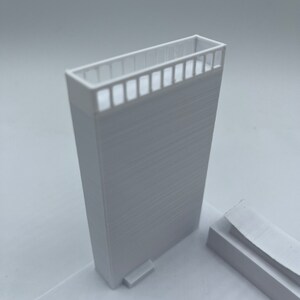 K&ouml;nnte beinhalten: Ein wei&szlig;es 3D-gedrucktes Modell eines Geb&auml;udes mit einem Balkon und einer kleinen Stufe, die zu ihm f&uuml;hrt.