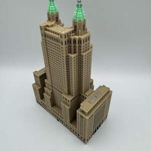 Może przedstawiać: Szczeg&oacute;łowy model wieżowca z beżową elewacją i dwiema wieżami zwieńczonymi zielenią. Budynek posiada liczne okna i detale architektoniczne, prezentujące klasyczny design. Model umieszczono na gładkim, białym tle.