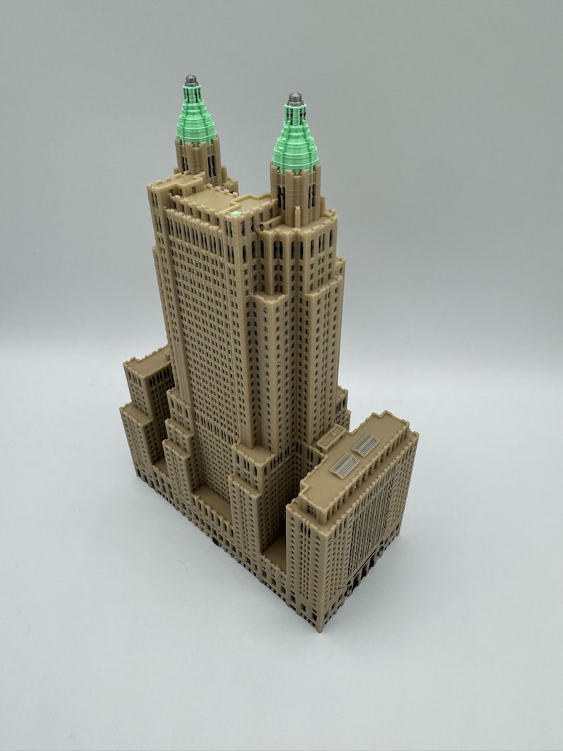 Może przedstawiać: Szczeg&oacute;łowy model wieżowca z beżową elewacją i dwiema wieżami zwieńczonymi zielenią. Budynek posiada liczne okna i detale architektoniczne, prezentujące klasyczny design. Model umieszczono na gładkim, białym tle.
