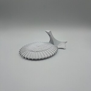 May include: A white 3D printed model of a modern building with a curved roof and a pointed spire.