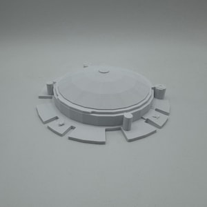May include: A light gray, 3D-printed model of a domed structure with a circular base. The dome has a series of geometric facets and a small, raised circular feature at the top. The base features rectangular cutouts and cylindrical supports.