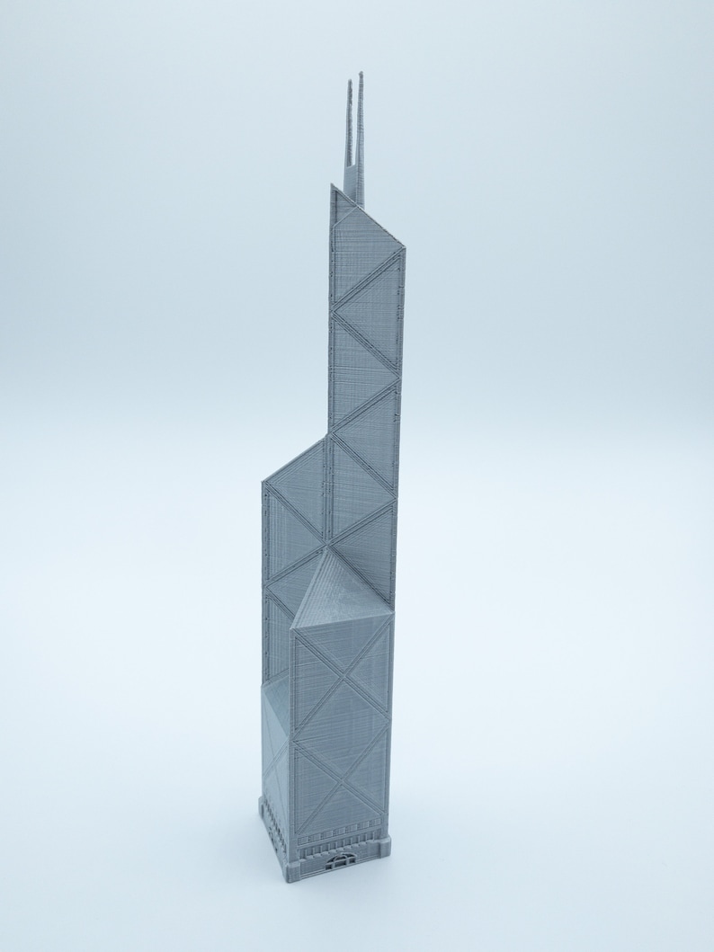 May include: A gray, 3D-printed model of a skyscraper with a distinctive geometric design. The building features a series of triangular and rectangular shapes, with two tall spires at the top. The model is set against a plain white background.