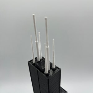 May include: A black 3D printed model of a skyscraper with white antenna details.