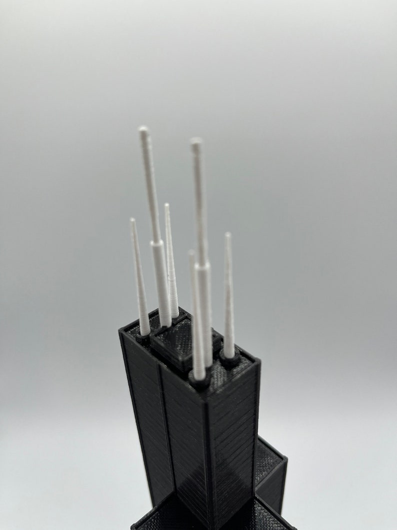 May include: A black 3D printed model of a skyscraper with white antenna details.