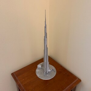 May include: A silver model of the Burj Khalifa, a skyscraper in Dubai, on a wooden table.