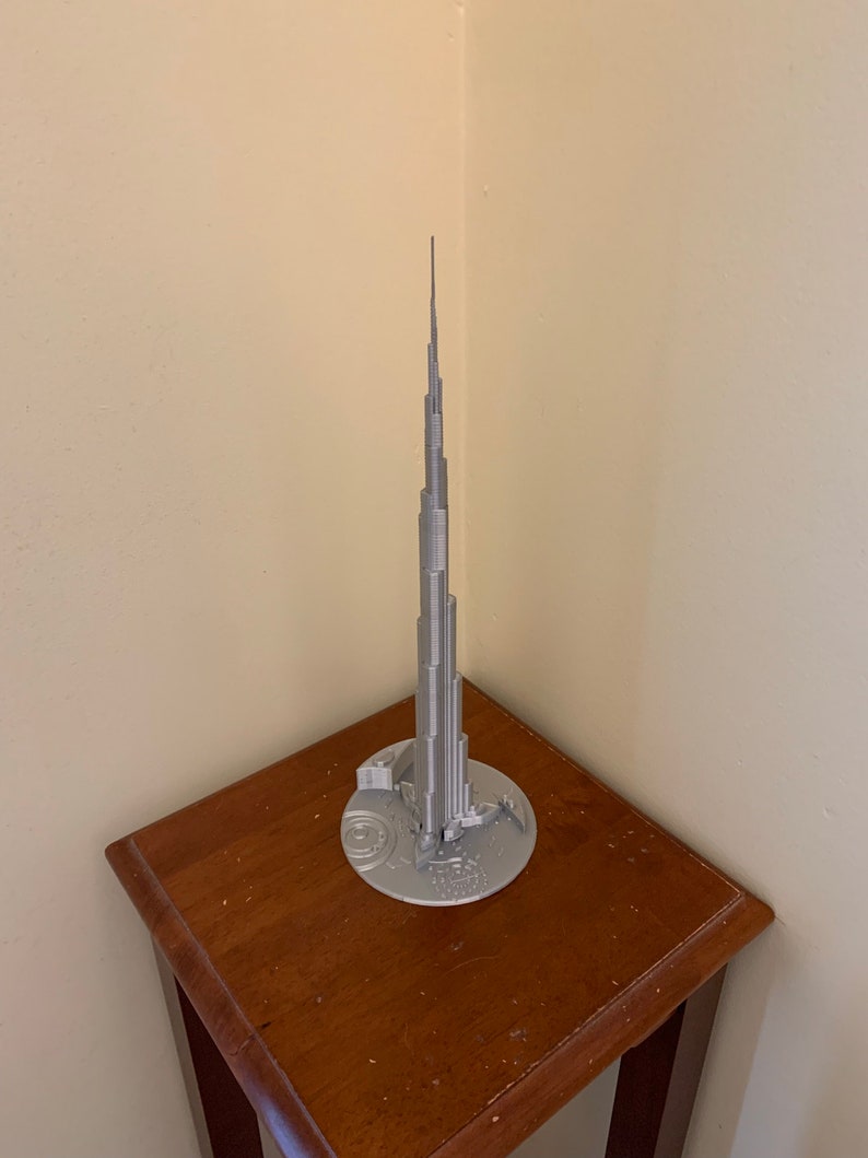 May include: A silver model of the Burj Khalifa, a skyscraper in Dubai, on a wooden table.