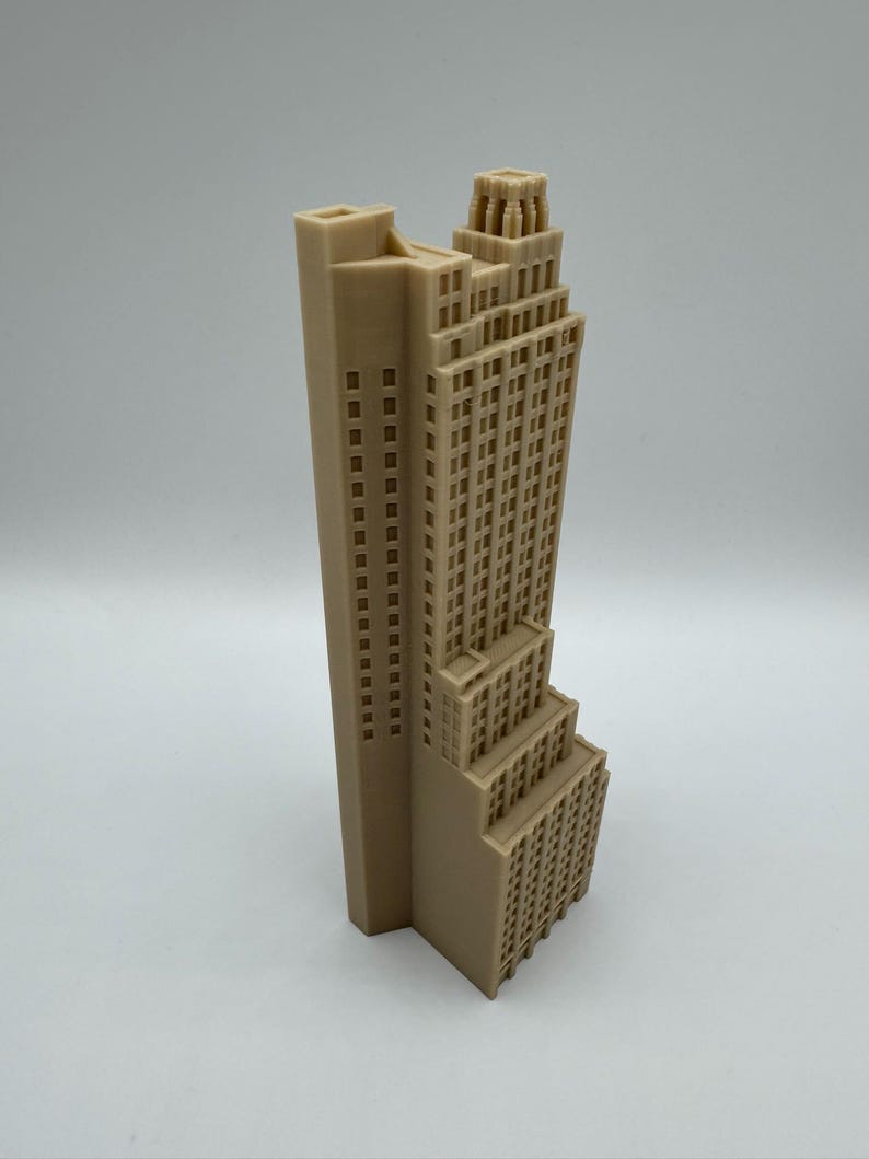 May include: A beige architectural model of a skyscraper. The building features a tall, rectangular tower with numerous windows, and a stepped design towards the base. The top of the building has a decorative crown.