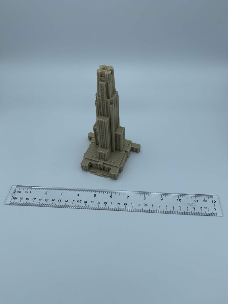 May include: A 3D printed model of a tall building with a pointed roof and many windows. The model is beige and is sitting on a white surface.