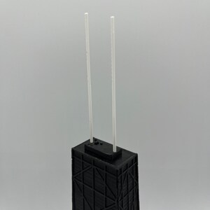 May include: A black architectural model of a skyscraper with two white antennae. The building has a geometric facade design and a flat roof. The model is set against a plain, light gray background.