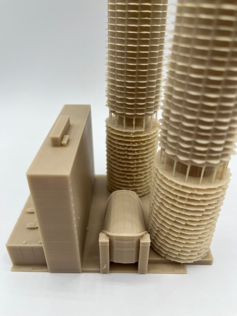May include: A 3D printed model of a building with two towers and a smaller building in the front. The towers are made of stacked rings and the smaller building has a rounded roof.