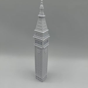 May include: A white 3D printed model of a tall building with a pointed roof and many windows.
