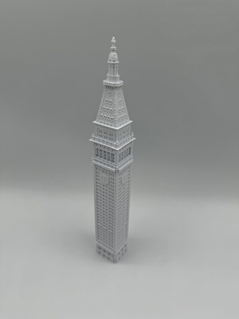 May include: A white 3D printed model of a tall building with a pointed roof and many windows.