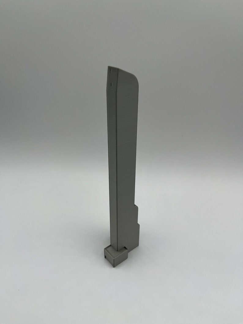 May include: A gray, 3D-printed architectural model of a skyscraper. The model has a rectangular base and a tall, slender body with a slightly curved top. The surface has a textured appearance.