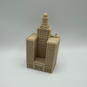 May include: A beige miniature model of a tall building with a tower on top. The building has many windows and is detailed with small architectural features.
