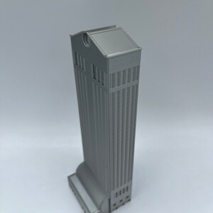 May include: A gray 3D printed model of a tall building with a flat roof and a rounded base.