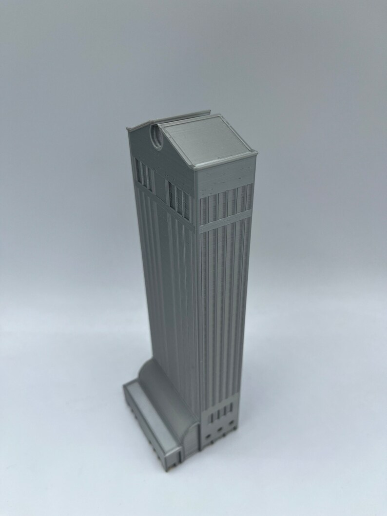 May include: A gray 3D printed model of a tall building with a flat roof and a rounded base.