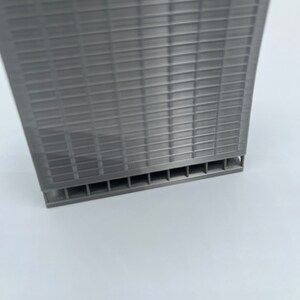 May include: A gray 3D printed model of a skyscraper with a grid pattern on the facade. The model has a base with a series of small openings.