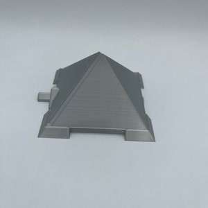 Puede incluir: Modelo de pir&aacute;mide gris impreso en 3D con una superficie texturizada. La pir&aacute;mide tiene una base rectangular con peque&ntilde;as extensiones rectangulares a cada lado. La parte superior de la pir&aacute;mide es un &aacute;pice puntiagudo.