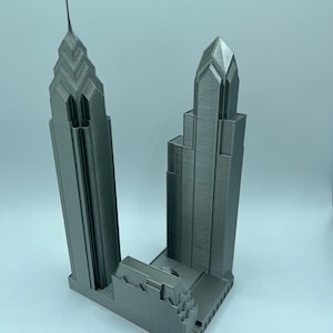 May include: A 3D printed model of two skyscrapers, one taller than the other, with a gray metallic finish.